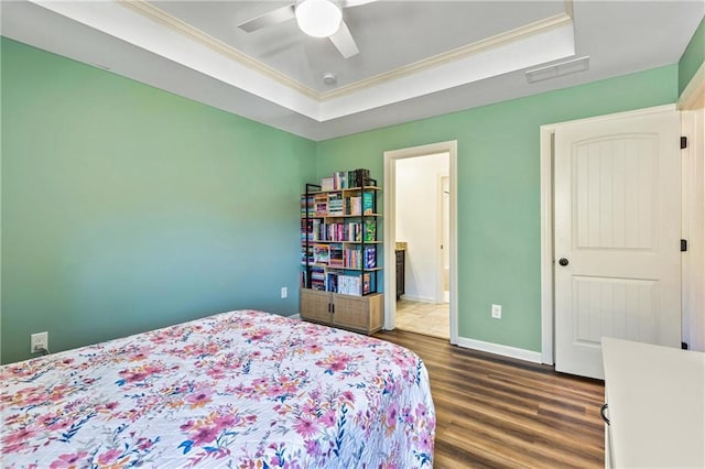 bedroom featuring baseboards, a raised ceiling, dark wood finished floors, ornamental molding, and ensuite bathroom