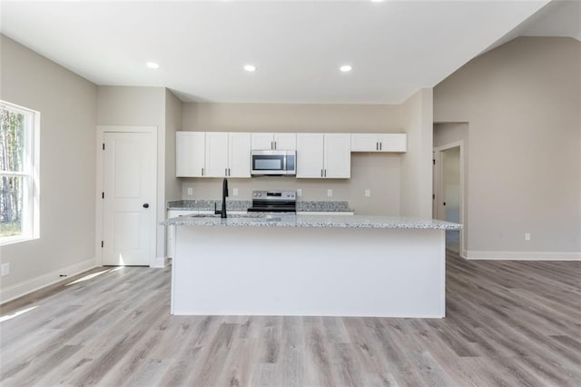 kitchen with white cabinets, appliances with stainless steel finishes, an island with sink, and baseboards