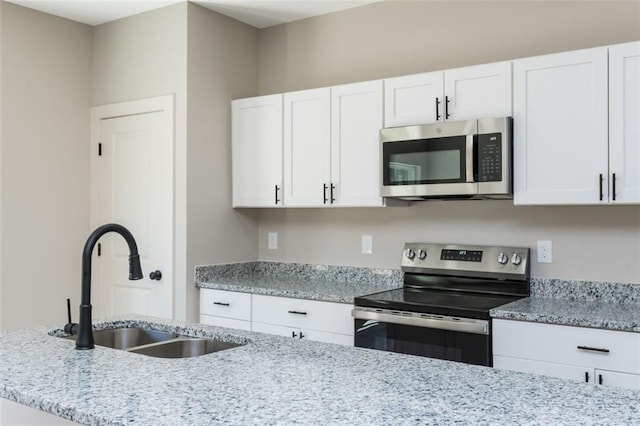 kitchen with white cabinetry, appliances with stainless steel finishes, light stone countertops, and a sink