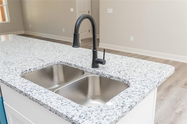 room details featuring a sink, baseboards, light stone counters, and wood finished floors