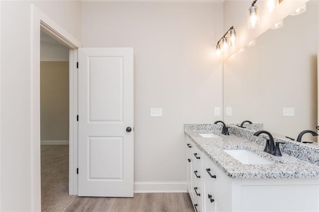 bathroom featuring double vanity, wood finished floors, baseboards, and a sink