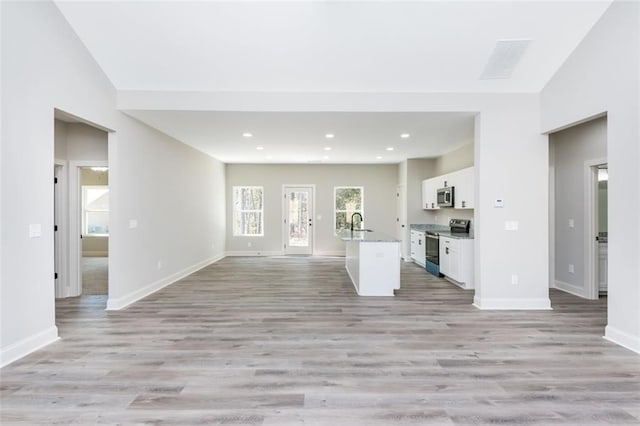 unfurnished living room with recessed lighting, baseboards, a sink, and light wood finished floors