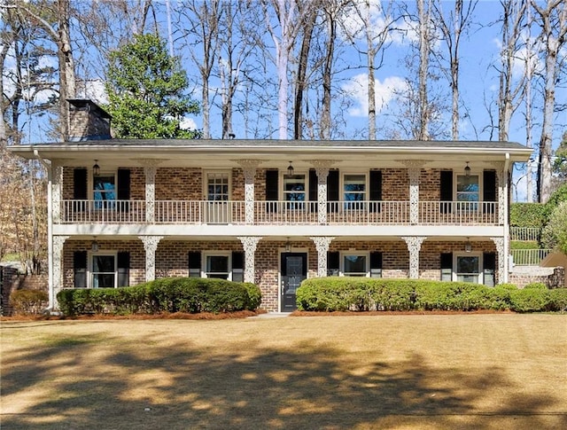 view of front of home featuring brick siding, a chimney, and a balcony