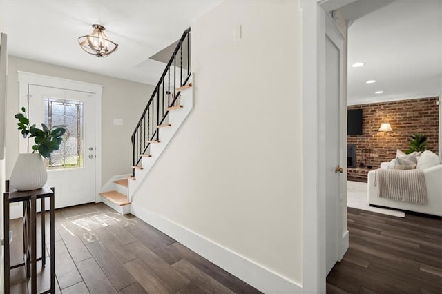 foyer with dark wood-style floors, brick wall, stairs, and baseboards