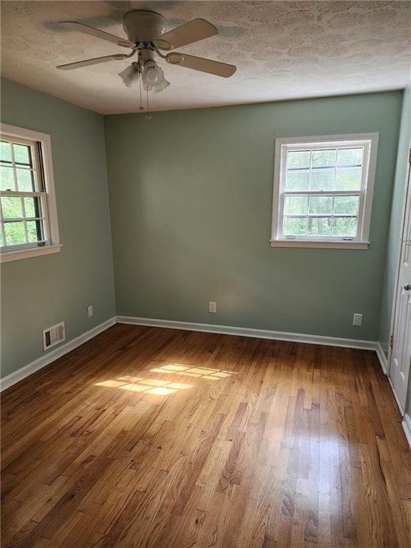 empty room featuring ceiling fan, plenty of natural light, and light wood-type flooring