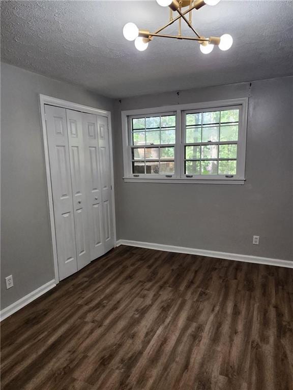 unfurnished bedroom with a closet, a textured ceiling, a chandelier, and dark hardwood / wood-style floors