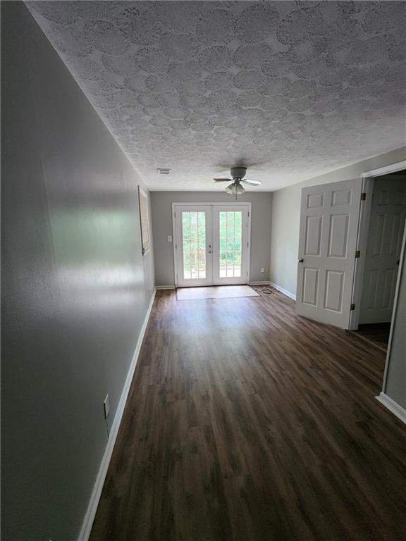 empty room featuring french doors, dark wood-type flooring, a textured ceiling, and ceiling fan