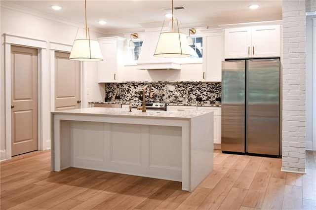 kitchen featuring light stone counters, a center island with sink, freestanding refrigerator, white cabinetry, and light wood-type flooring