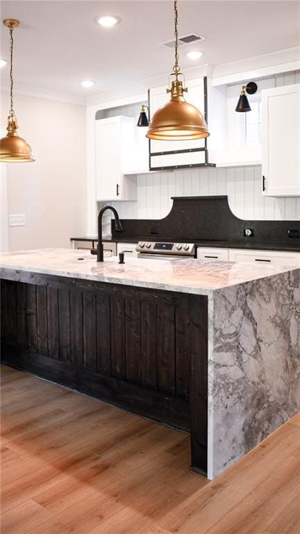 kitchen with light wood finished floors, visible vents, crown molding, hanging light fixtures, and white cabinetry