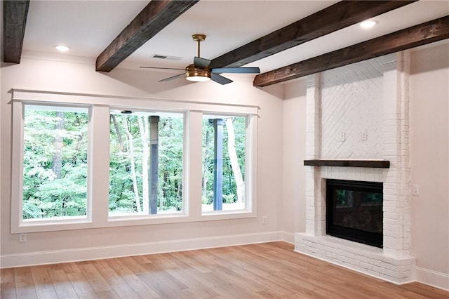 unfurnished living room with wood finished floors, visible vents, baseboards, beam ceiling, and a fireplace