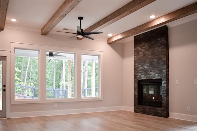 unfurnished living room with a tiled fireplace, beam ceiling, plenty of natural light, and baseboards