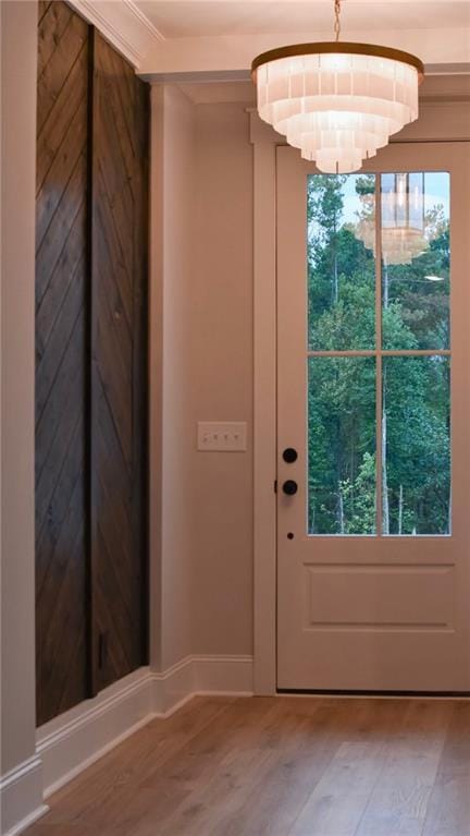 doorway to outside featuring baseboards, an inviting chandelier, wood finished floors, and a healthy amount of sunlight