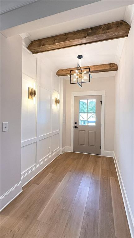 doorway featuring an inviting chandelier, beam ceiling, wood finished floors, and baseboards