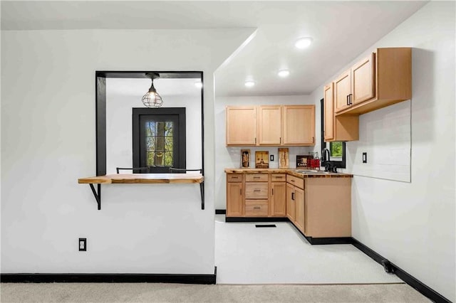 kitchen with baseboards, recessed lighting, light brown cabinets, and a sink