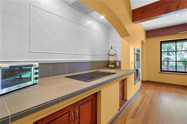 4043 Piedmont Lake Rd, Pine Mountain, GA 31822 - kitchen featuring black electric stovetop, tile counters, light wood-type flooring, arched walkways, and beamed ceiling