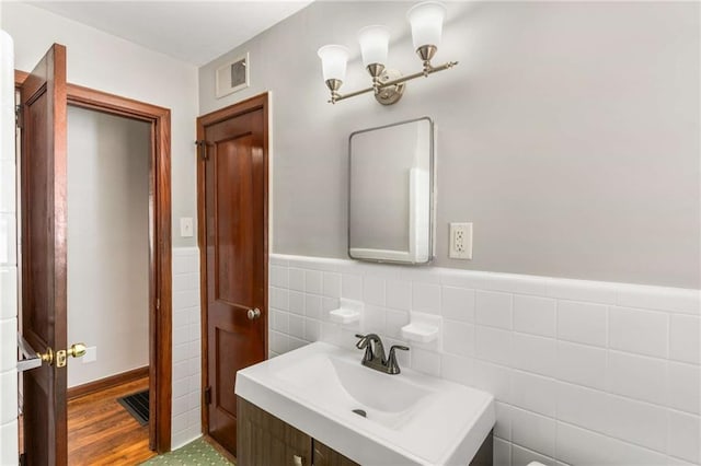 bathroom featuring visible vents, tile walls, a wainscoted wall, and a sink