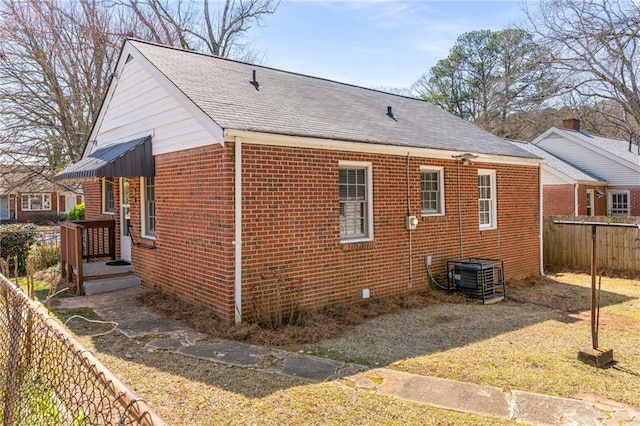 view of property exterior with central AC unit, fence, brick siding, and a shingled roof