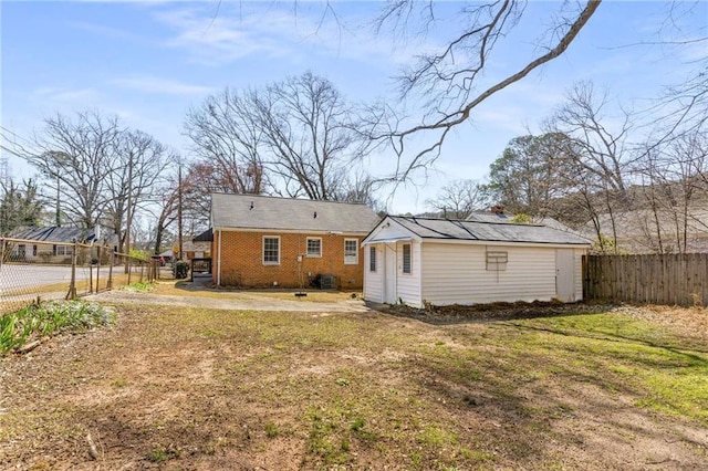 back of house featuring a lawn, fence, an outdoor structure, brick siding, and central AC unit