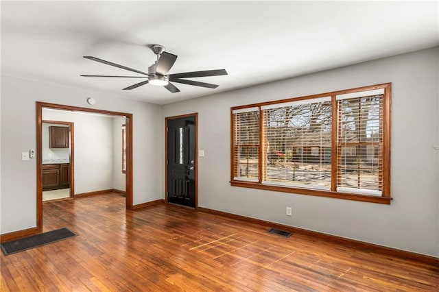 empty room with visible vents, a ceiling fan, baseboards, and hardwood / wood-style flooring