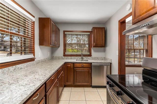 kitchen with under cabinet range hood, light tile patterned floors, light stone counters, appliances with stainless steel finishes, and a sink