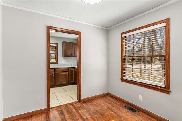 spare room with visible vents, crown molding, light wood-type flooring, and baseboards