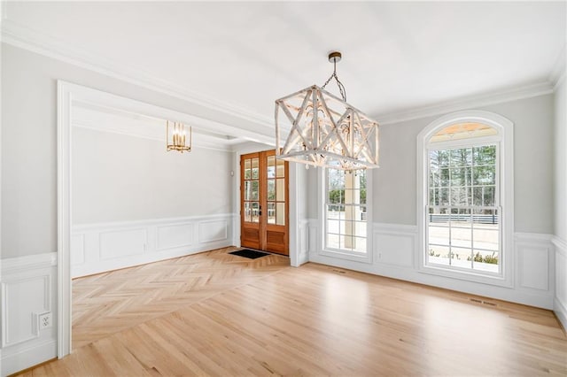 unfurnished dining area with light parquet flooring, ornamental molding, and a chandelier