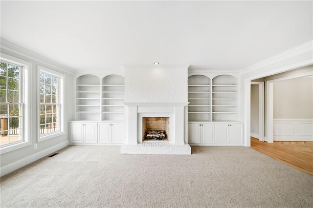 unfurnished living room with light carpet, crown molding, a fireplace, and built in shelves