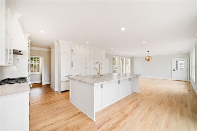 kitchen with white cabinetry, a wealth of natural light, ornamental molding, and an island with sink