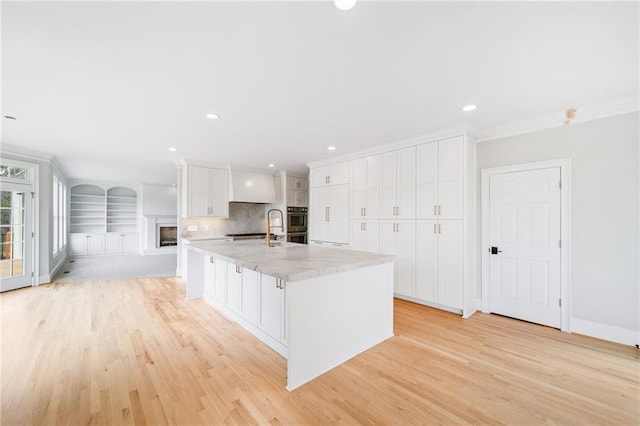 kitchen with crown molding, a spacious island, light stone countertops, white cabinets, and light wood-type flooring