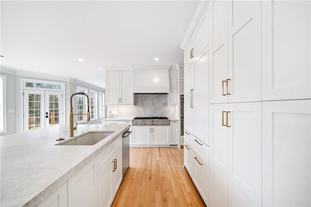 kitchen featuring tasteful backsplash, white cabinetry, sink, wall chimney range hood, and french doors