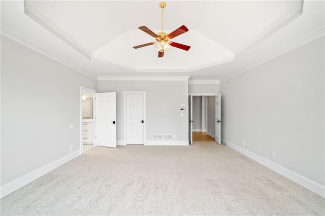 unfurnished bedroom with crown molding, connected bathroom, a tray ceiling, and light colored carpet