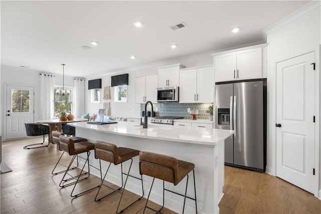 kitchen featuring a kitchen island with sink, a kitchen bar, white cabinetry, and appliances with stainless steel finishes