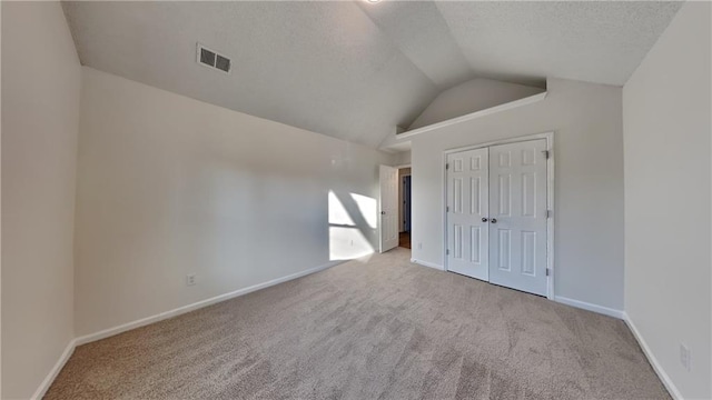 unfurnished bedroom featuring vaulted ceiling, light colored carpet, a textured ceiling, and a closet