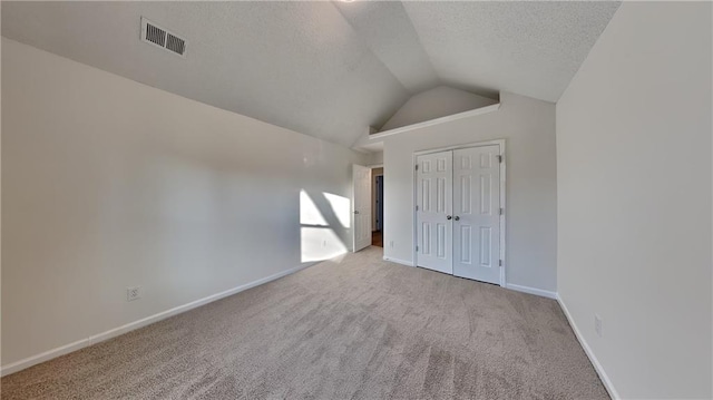 unfurnished bedroom featuring a closet, light colored carpet, vaulted ceiling, and a textured ceiling