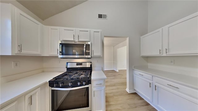 kitchen with stainless steel appliances, white cabinets, high vaulted ceiling, and light hardwood / wood-style flooring