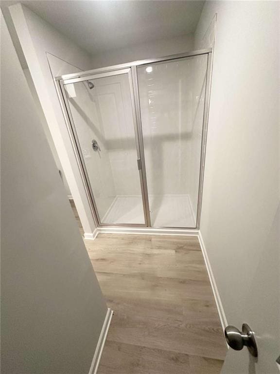 full bath with a stall shower, wood finished floors, and baseboards