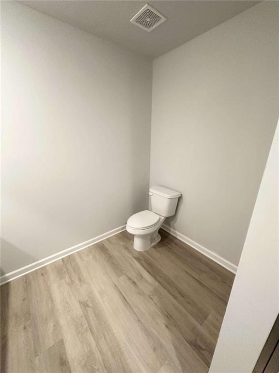 half bathroom featuring toilet, wood finished floors, visible vents, and baseboards