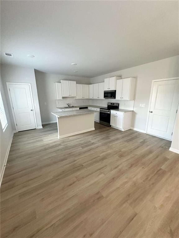 kitchen with an island with sink, stainless steel electric stove, light countertops, light wood-style floors, and white cabinetry