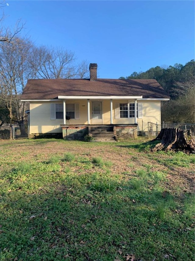 back of house featuring a yard, covered porch, a chimney, and fence