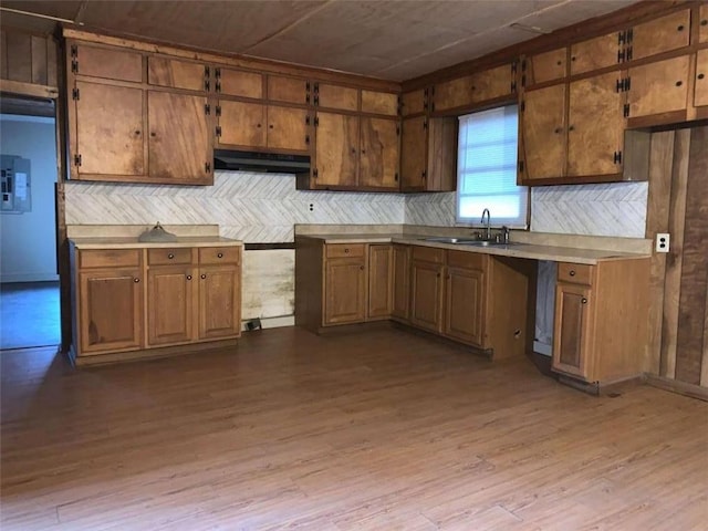 kitchen with brown cabinetry, wood finished floors, a sink, light countertops, and under cabinet range hood