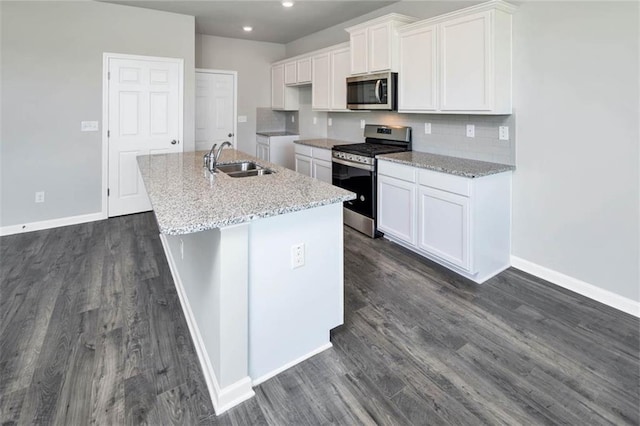 kitchen featuring a sink, white cabinets, appliances with stainless steel finishes, backsplash, and a center island with sink