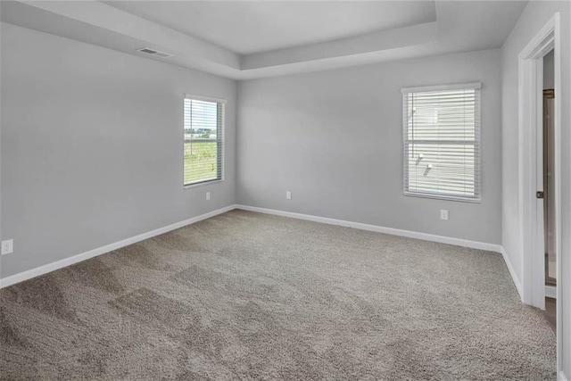 empty room featuring carpet floors, a tray ceiling, visible vents, and baseboards