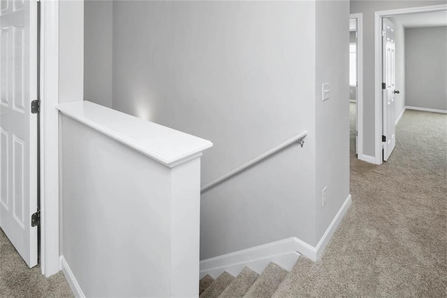 hallway featuring carpet, baseboards, and an upstairs landing