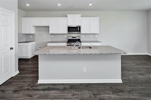 kitchen with a center island with sink, light stone countertops, stainless steel appliances, white cabinetry, and a sink