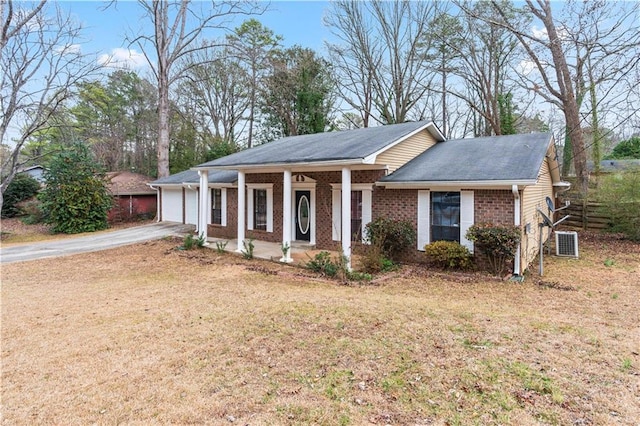 ranch-style house featuring a garage, covered porch, a front yard, and central air condition unit