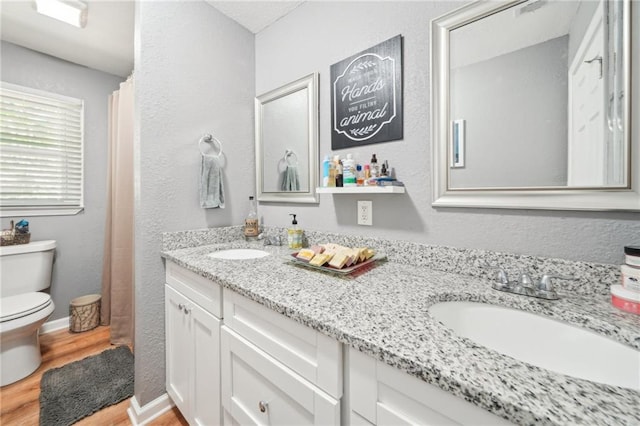 full bath with toilet, wood finished floors, double vanity, a textured wall, and curtained shower