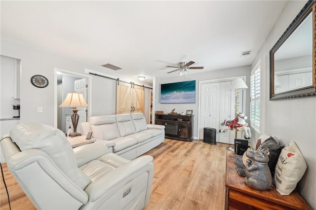 living area featuring a barn door, a ceiling fan, and light wood-style flooring