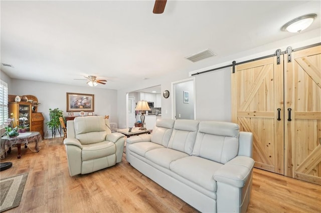 living area with a ceiling fan, a barn door, and light wood-type flooring