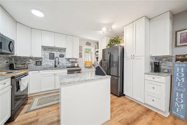 kitchen with appliances with stainless steel finishes, tasteful backsplash, a kitchen island, white cabinets, and a sink