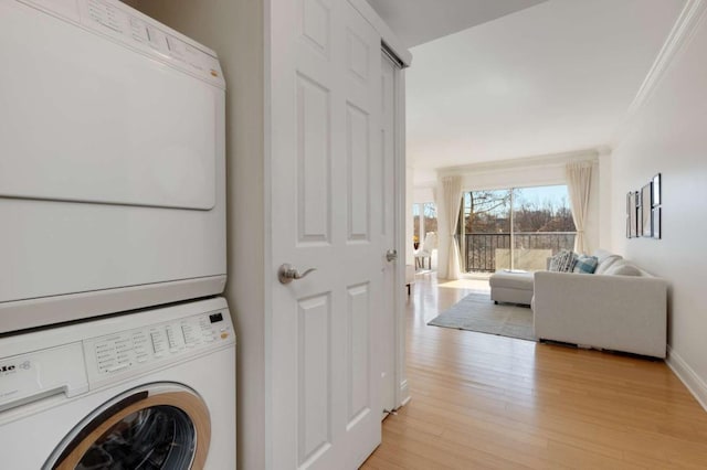 laundry room with stacked washer / dryer, baseboards, light wood-type flooring, ornamental molding, and laundry area